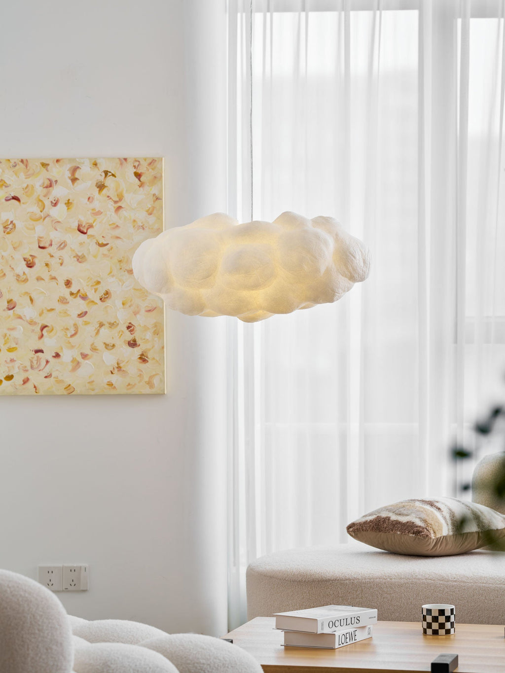 Cushions and a sheer curtain sit beneath this lit Clérachic cloud-shaped pendant near a framed print.