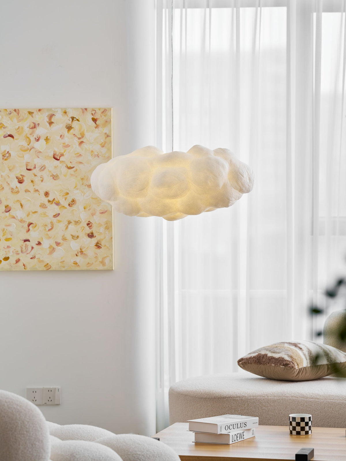 Cushions and a sheer curtain sit beneath this lit Clérachic cloud-shaped pendant near a framed print.