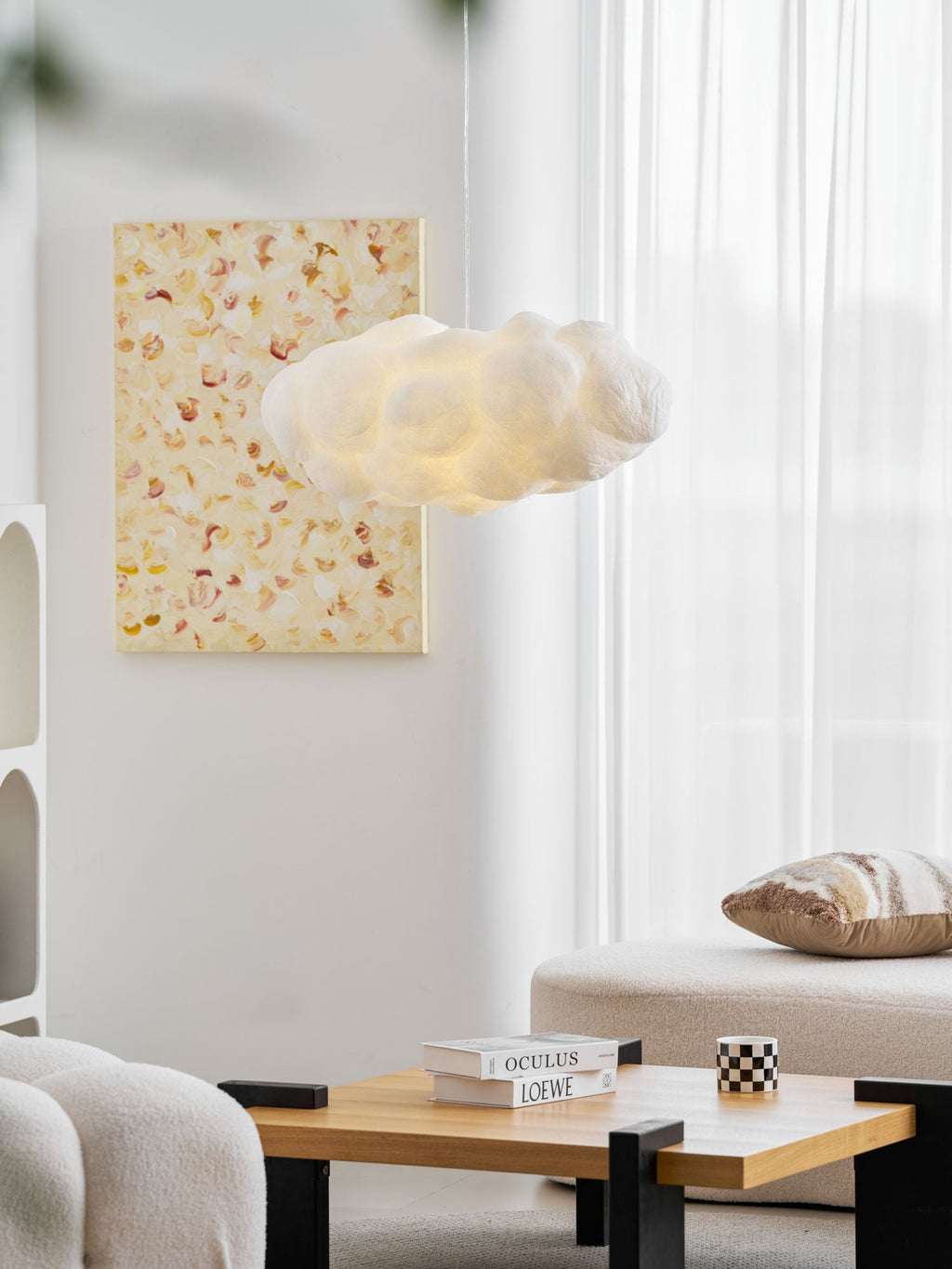This Clérachic cloud-shaped pendant glows near a framed print above a wood coffee table stacked with books.