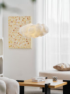 This Clérachic cloud-shaped pendant glows near a framed print above a wood coffee table stacked with books.