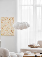 Unlit, this Clérachic cloud-shaped pendant hangs beside a framed floral print near a sheer curtain.