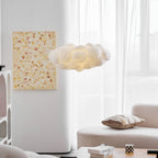 This Clérachic cloud-shaped pendant glows beside a framed print, a cushioned sofa and sheer curtains.