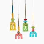 Four Clérachic pendants in amber, coral, green and teal glass hang at staggered lengths, shown on white.
