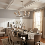 Under a coffered ceiling with grey walls, the nickel finish of this Clérachic chandelier lights a long dining table.
