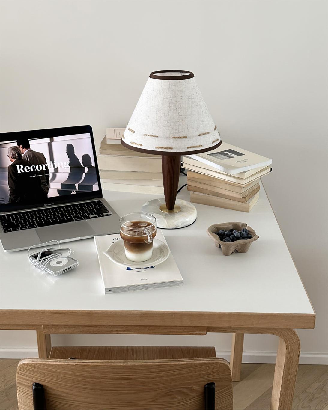 Clérachic lamp lit on a white desk beside an open laptop, stacked books and a cup of coffee.