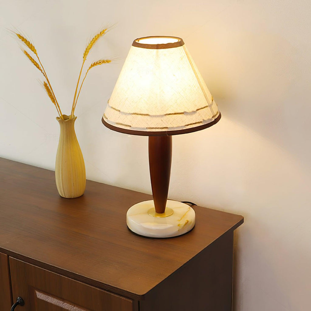 Close view of the lit Clérachic lamp on a sideboard, its trimmed linen shade beside a vase of dried wheat stalks.