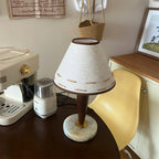 Clérachic lamp glowing on a round table in a cosy corner with a coffee maker, open book and chair nearby.