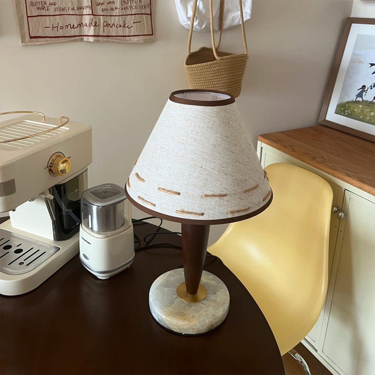 Clérachic lamp glowing on a round table in a cosy corner with a coffee maker, open book and chair nearby.
