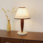 Lit Clérachic table lamp beside a dried-wheat vase on a walnut sideboard, its linen shade glowing warm against a cream wall.