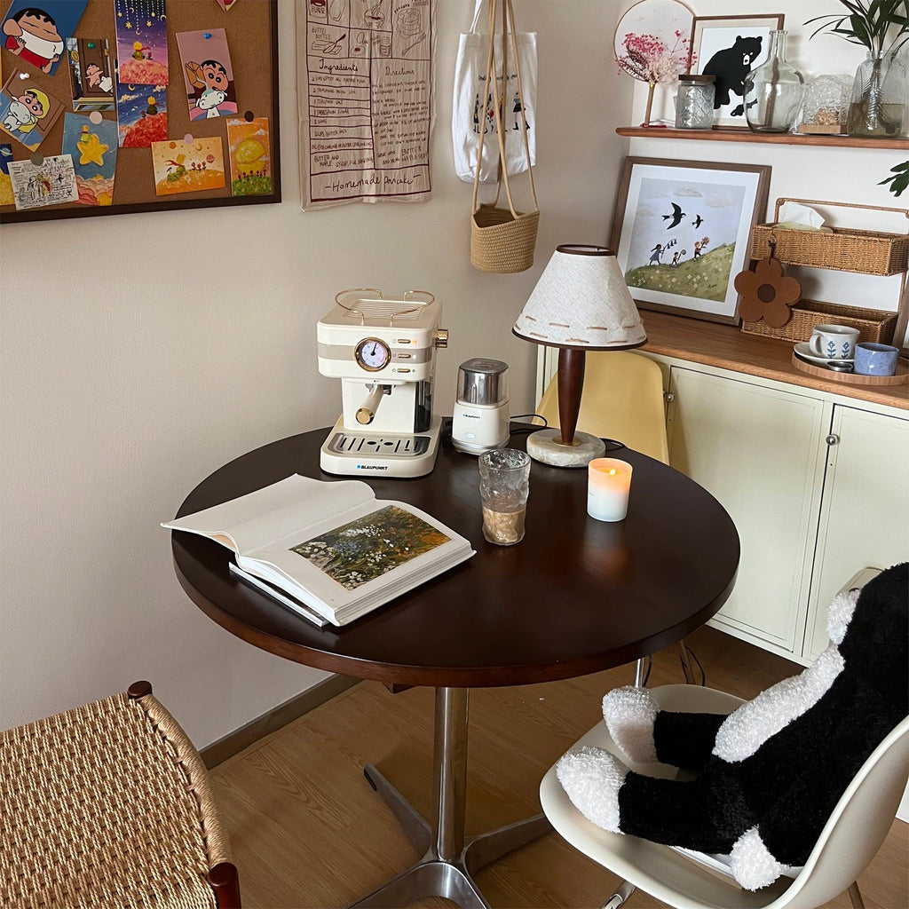 Clérachic lamp lit on a round table beside a coffee maker, framed art and a wicker basket hanging on the wall.