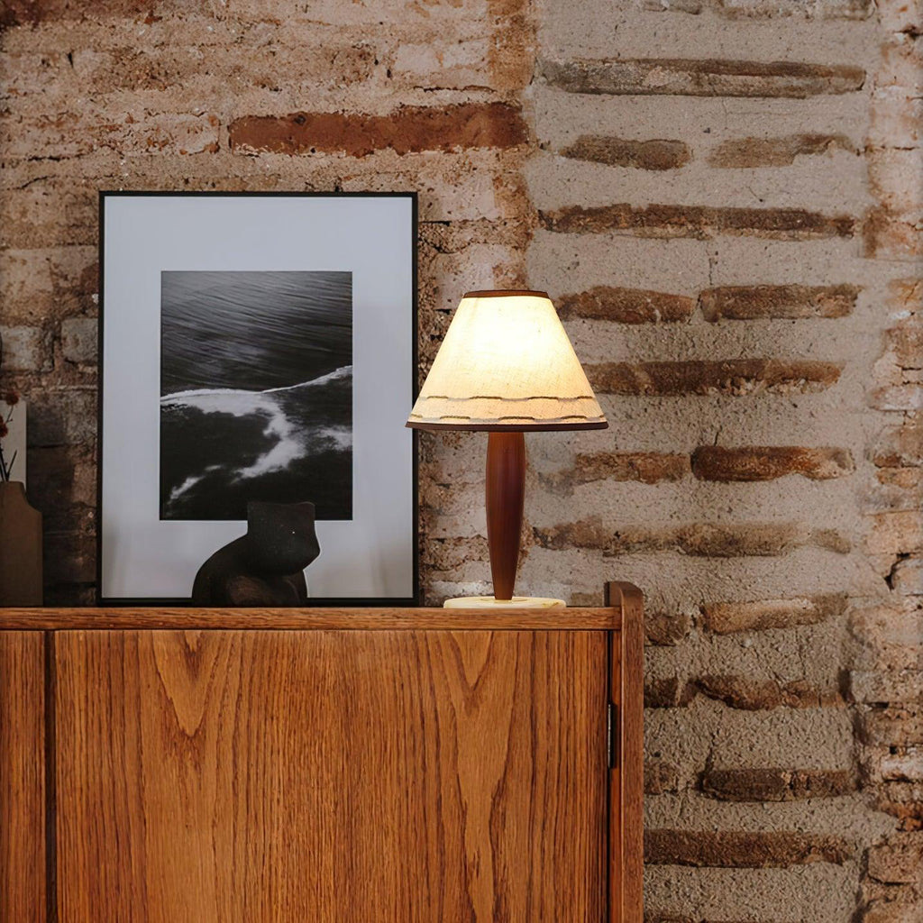 Small Clérachic lamp glowing on a wooden cabinet set against an exposed brick wall, beside a framed photograph.