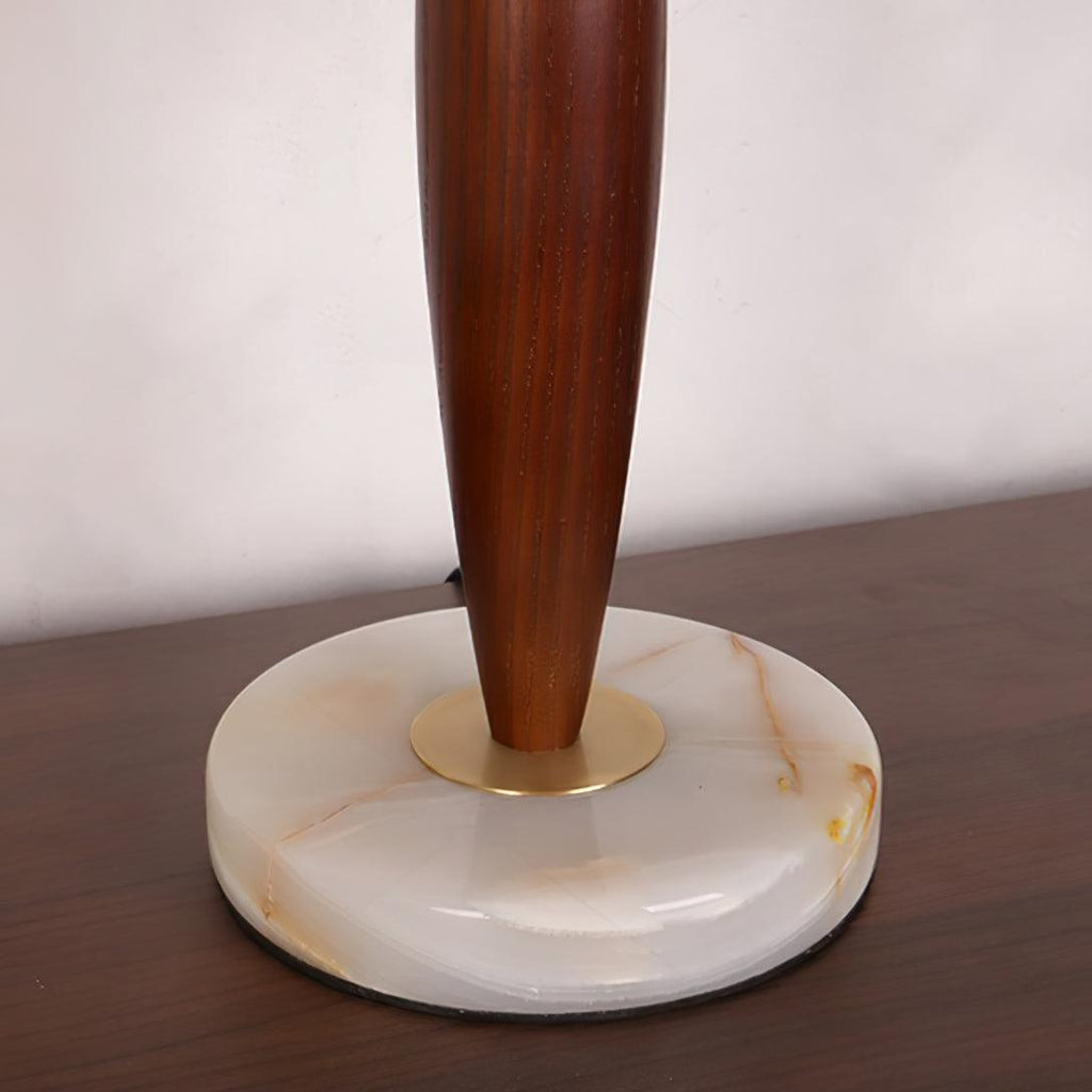 Close-up of the Clérachic lamp's tapered walnut stem meeting its round marble base at a brass collar.
