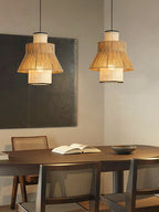 Two Clérachic pendants glow warm above a wood dining table set with an open book and a bowl, beneath an abstract canvas.