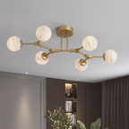 Mounted flush to a grey ceiling, this brass Clérachic chandelier branches six arms tipped with alabaster balls.