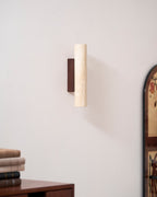 This Clérachic wall light, unlit, above a dresser stacked with books beside a floral-patterned mirror.