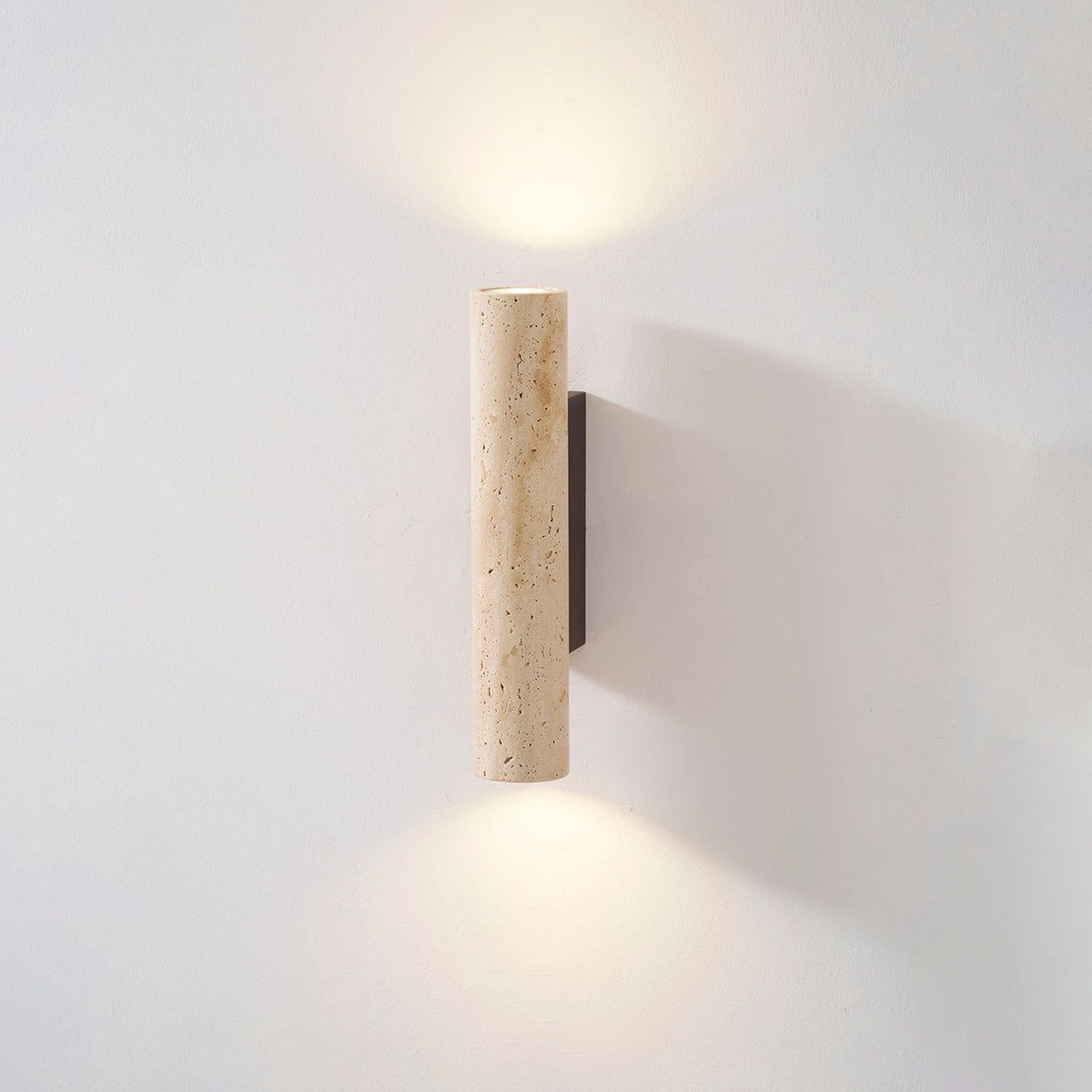 This shorter Clérachic wall light glows lit in the studio, set against a grey backdrop.