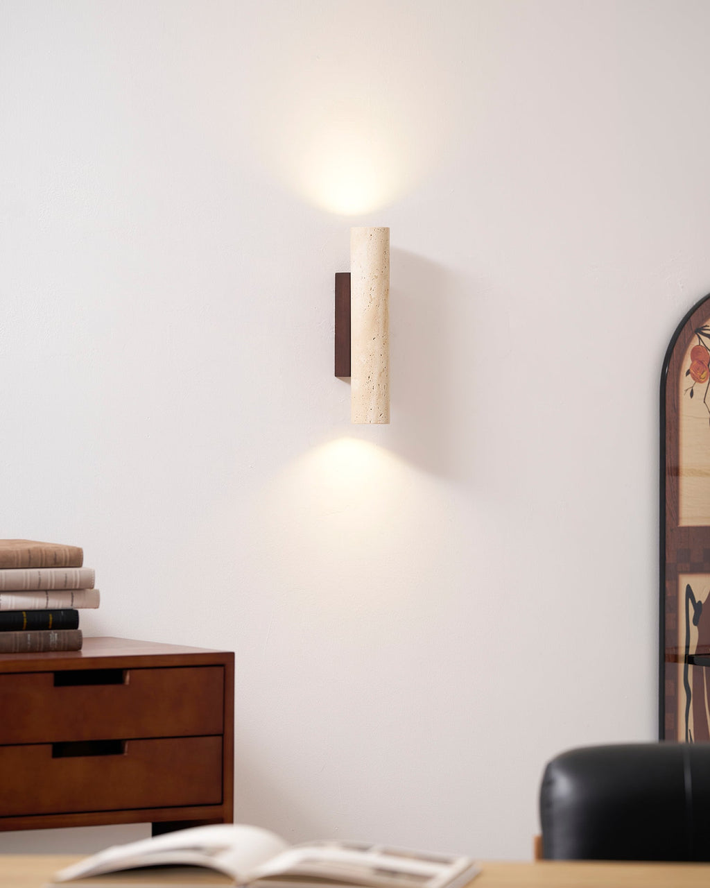A wood dresser stacked with books sits below this Clérachic wall light, lit, beside an arched mirror.