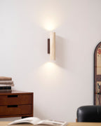 A wood dresser stacked with books sits below this Clérachic wall light, lit, beside an arched mirror.