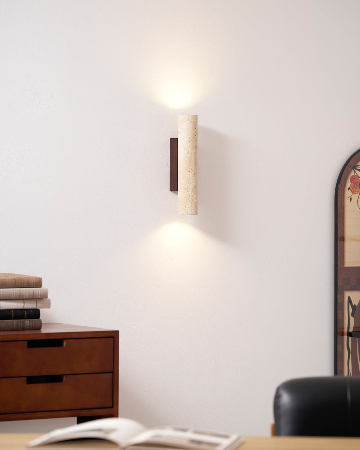A wood dresser stacked with books sits below this Clérachic wall light, lit, beside an arched mirror.