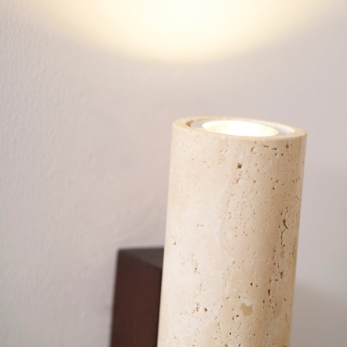 Close view of the base of this Clérachic wall light, showing the light source through travertine stone.