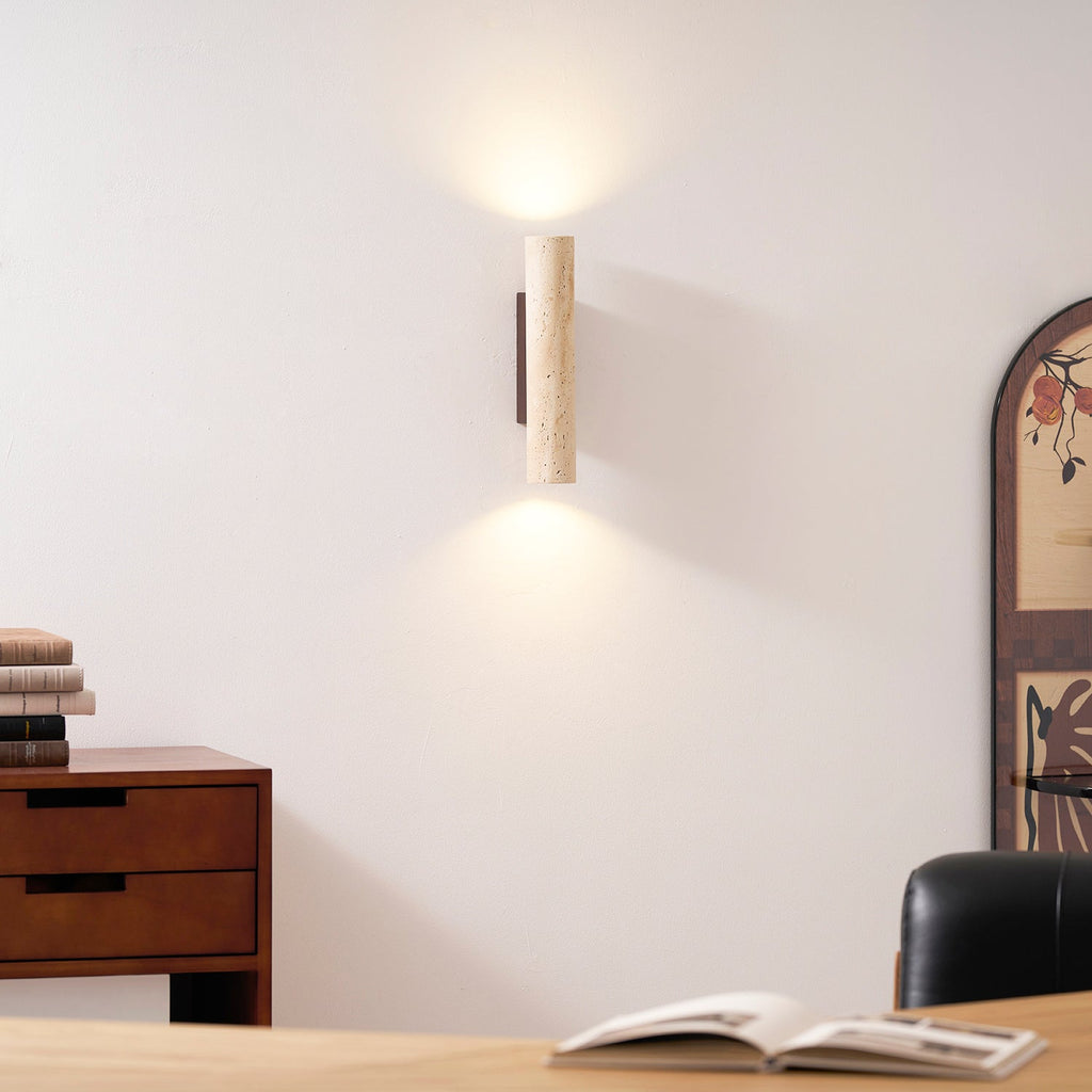 Stacked books top the wood dresser beneath this Clérachic wall light, lit, near a patterned mirror.