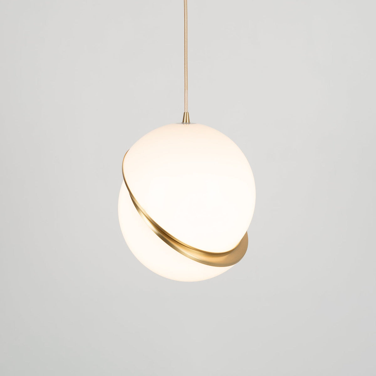 Turned slightly to the side, this Clérachic pendant's brass crescent shows at an angle against a grey backdrop.