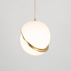 This Clérachic pendant's brass crescent sits low on the sphere, tilted gently against a plain grey backdrop.