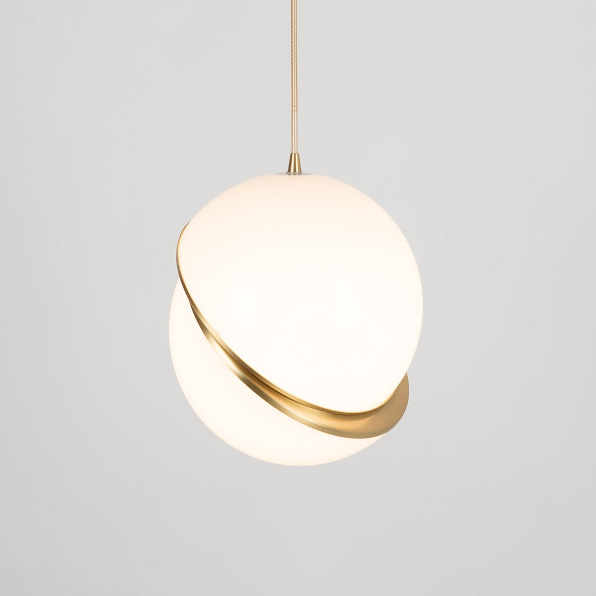 This Clérachic pendant's brass crescent sits low on the sphere, tilted gently against a plain grey backdrop.