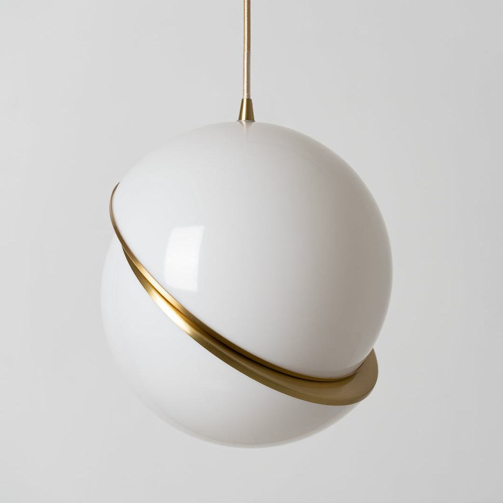 Photographed close up, this Clérachic pendant's glossy opal sphere fills most of the frame, brass crescent glinting.