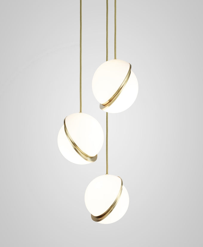 At staggered heights against a plain grey backdrop, three brass-crescent pendants cascade, from Clérachic.