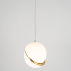 This Clérachic pendant hangs centred on a long brass cord, mid-size against a plain grey backdrop.