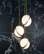 Three opal pendants with brass crescents cluster against a dark blue-grey marble tile wall, from Clérachic.