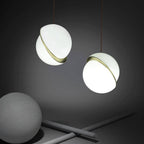 Against a charcoal backdrop, two brass-banded opal spheres hang beside a matte grey ball and crossed rods, from Clérachic.