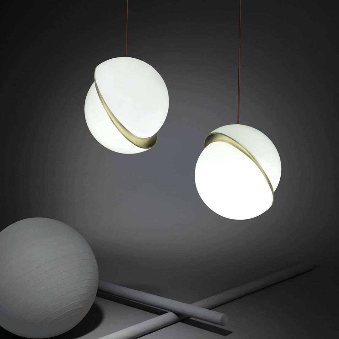 Against a charcoal backdrop, two brass-banded opal spheres hang beside a matte grey ball and crossed rods, from Clérachic.