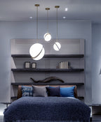 Above a bookshelf and navy bedspread in this styled bedroom, pendants of varying heights hang, from Clérachic.
