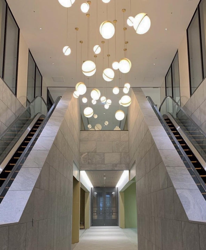 Down a stairwell beside an escalator, rows of opal pendants with brass crescents descend, from this Clérachic fixture.