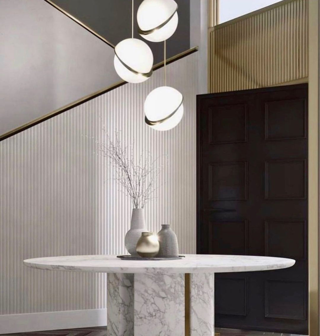 Down a stairwell beside a panelled brass handrail, three brass-crescent pendants cascade, from Clérachic.
