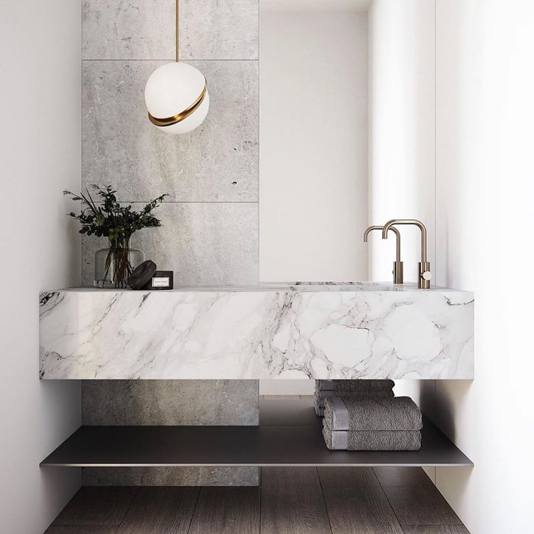 Above a marble vanity with brass tapware and folded grey towels, a single Clérachic pendant hangs.
