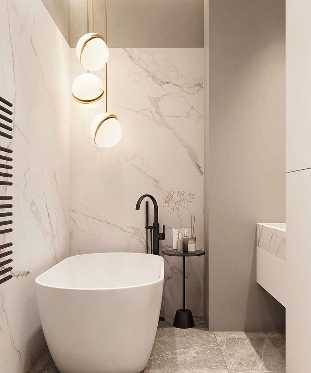 Beside a freestanding tub in a marble-clad bathroom, three brass-crescent pendants hang, from Clérachic.