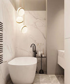 Beside a freestanding tub in a marble-clad bathroom, three brass-crescent pendants hang, from Clérachic.
