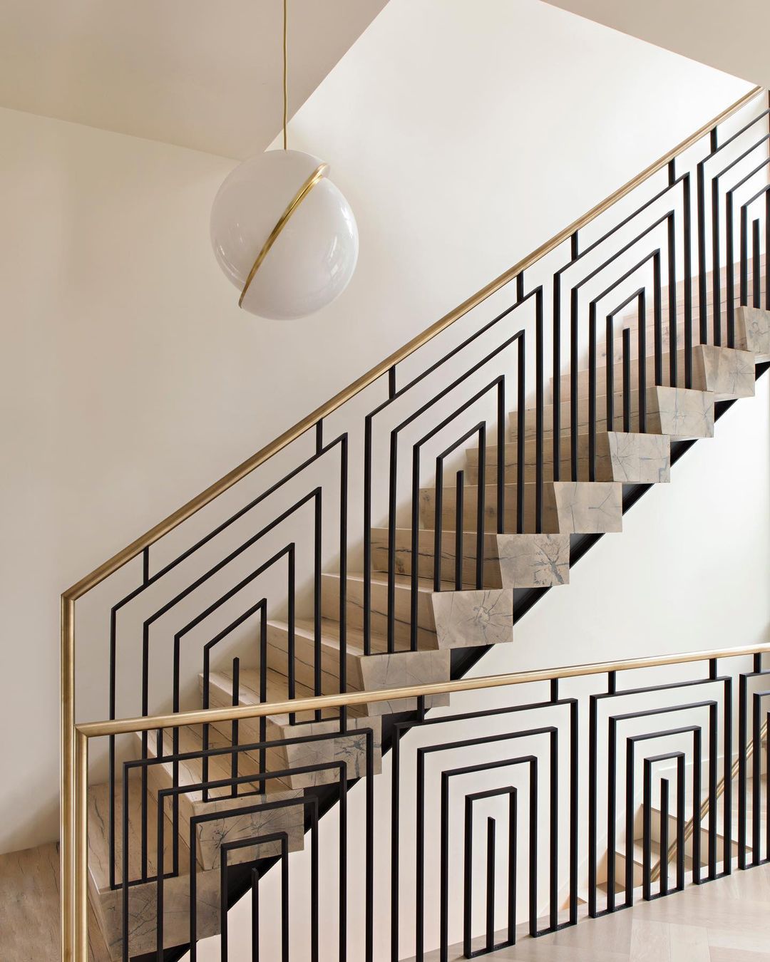 Beside a geometric black and brass stair rail, a single Clérachic pendant hangs.