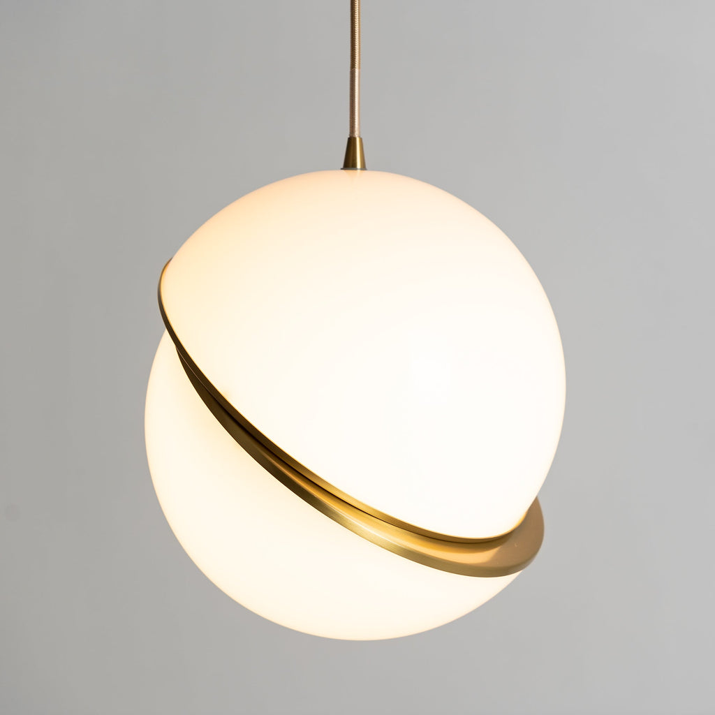 Front-on against a plain grey backdrop, this Clérachic pendant shows its brass crescent set on the diagonal.
