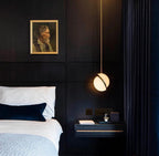 Beside a framed portrait, a Clérachic pendant lights a bedside nook, its brass crescent catching the glow.
