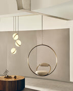 Beside a brass hoop chair on a soft pink backdrop, clustered pendants hang from this Clérachic fixture.