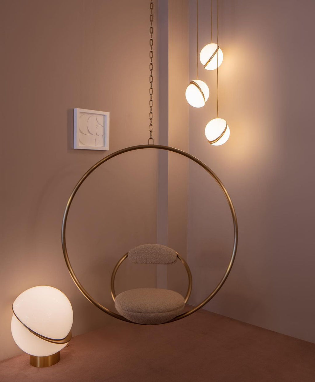 Framing a brass hoop chair on a dusky pink backdrop, clustered Clérachic pendants and a matching table lamp glow.