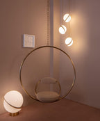 Framing a brass hoop chair on a dusky pink backdrop, clustered Clérachic pendants and a matching table lamp glow.