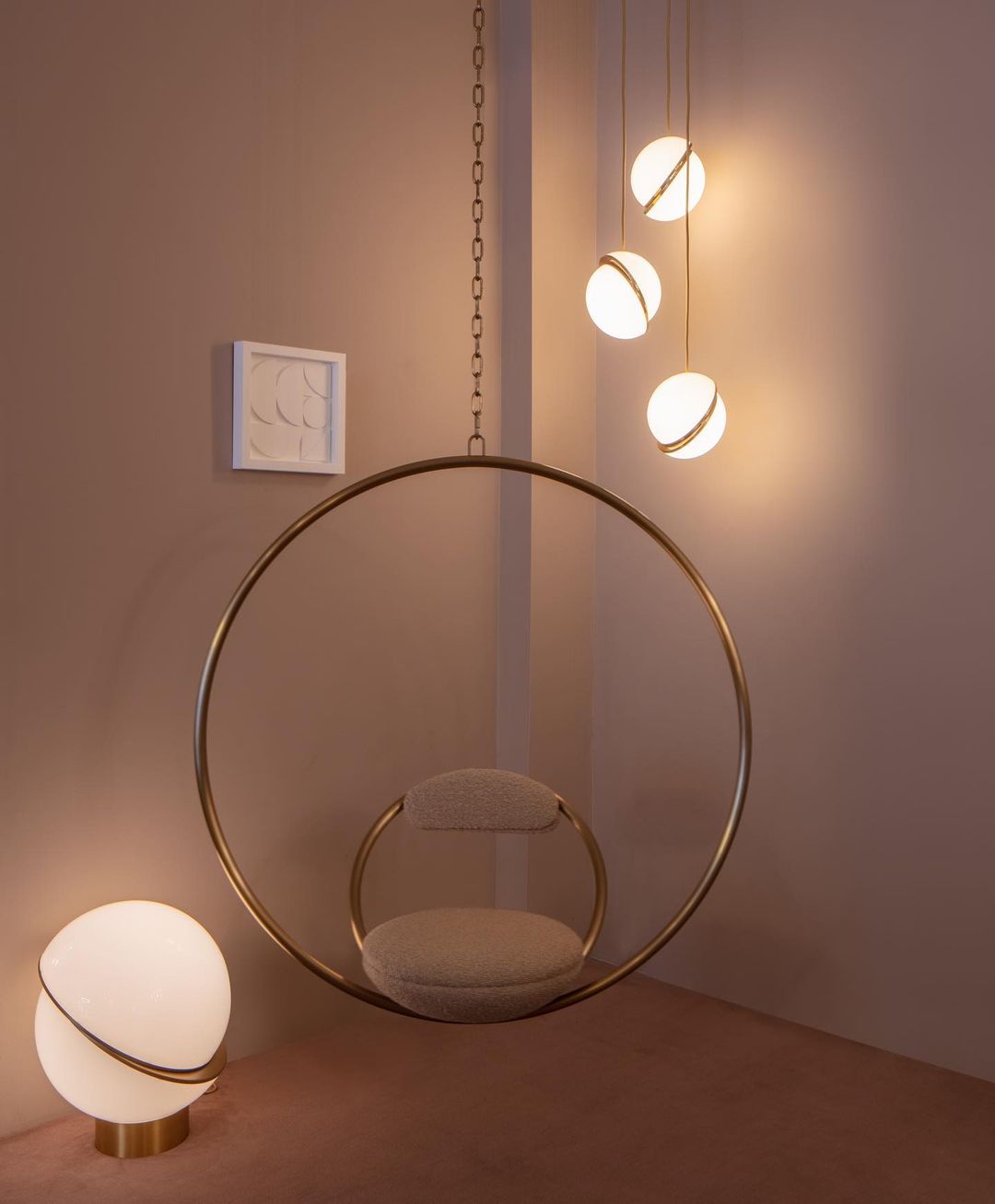 Framing a brass hoop chair on a dusky pink backdrop, clustered Clérachic pendants and a matching table lamp glow.
