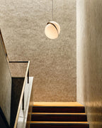 Above a textured gold stair wall, a single Clérachic pendant hangs.