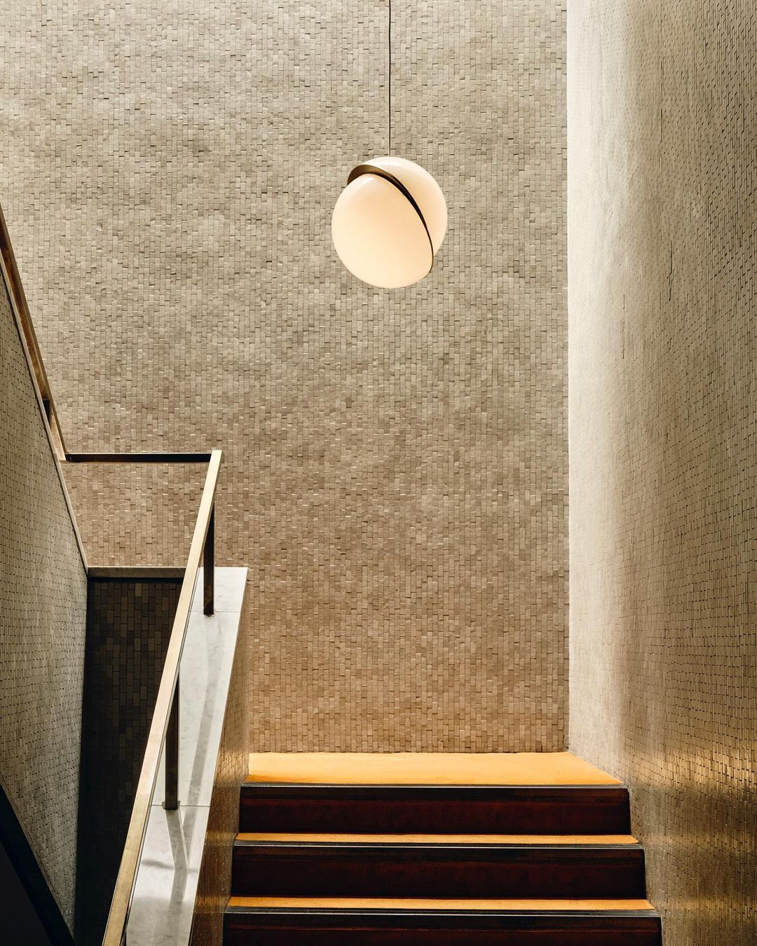 Above a textured gold stair wall, a single Clérachic pendant hangs.