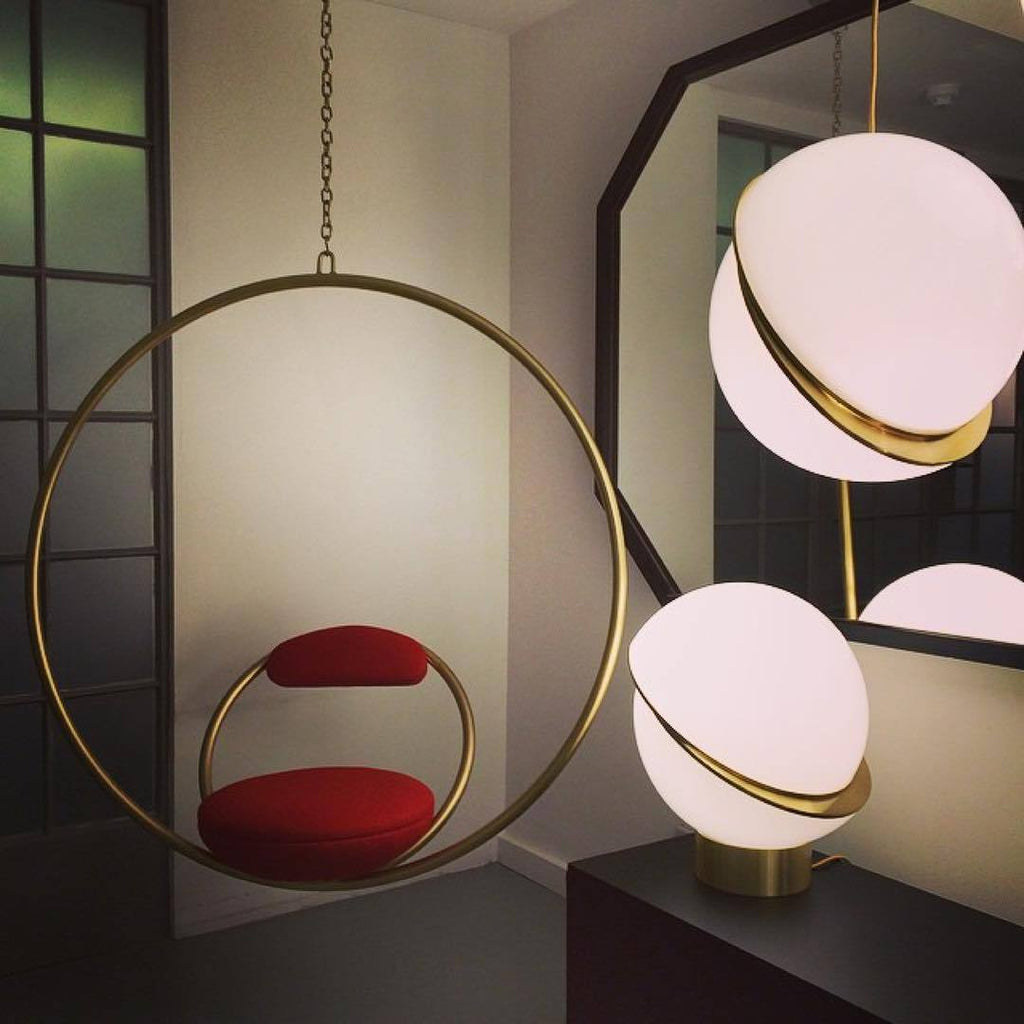 Reflected in a mirror beside a brass hoop chair, this Clérachic pendant and a matching table lamp glow.